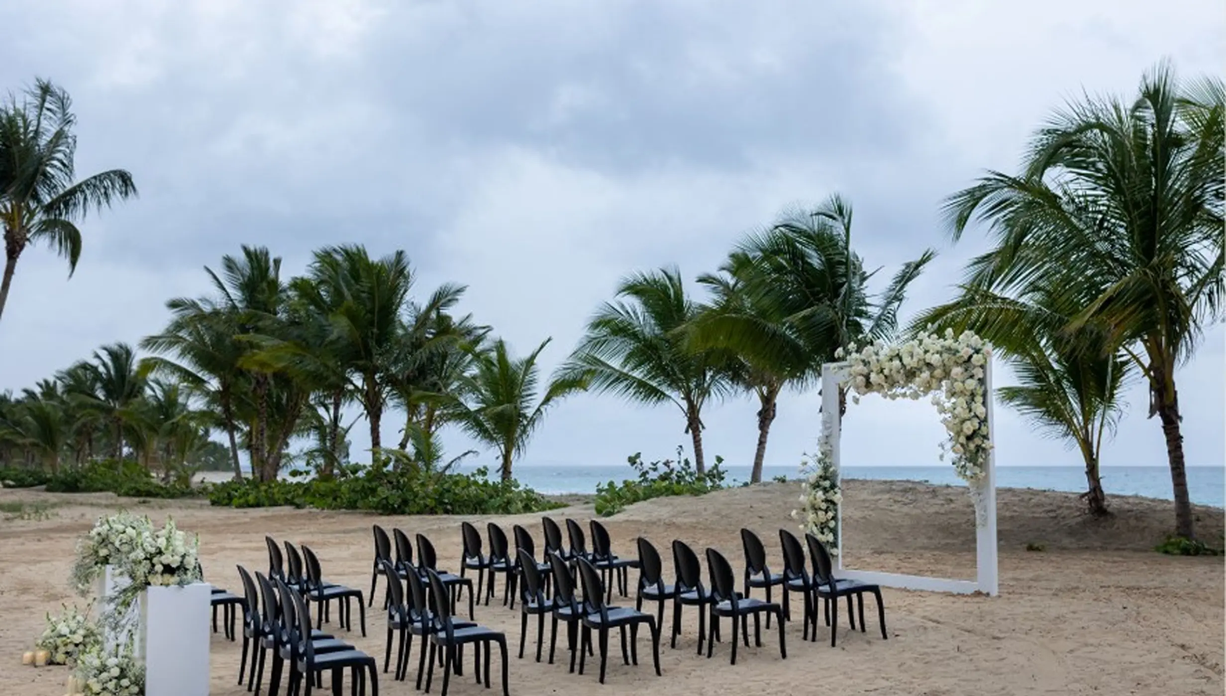 Beachfront wedding ceremony setup with white floral arch and black chairs at Dreams Playa Esmeralda, Miches