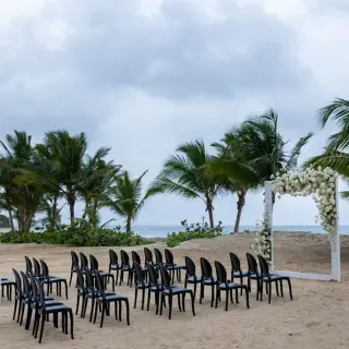 Beachfront wedding ceremony setup with white floral arch and black chairs at Dreams Playa Esmeralda, Miches