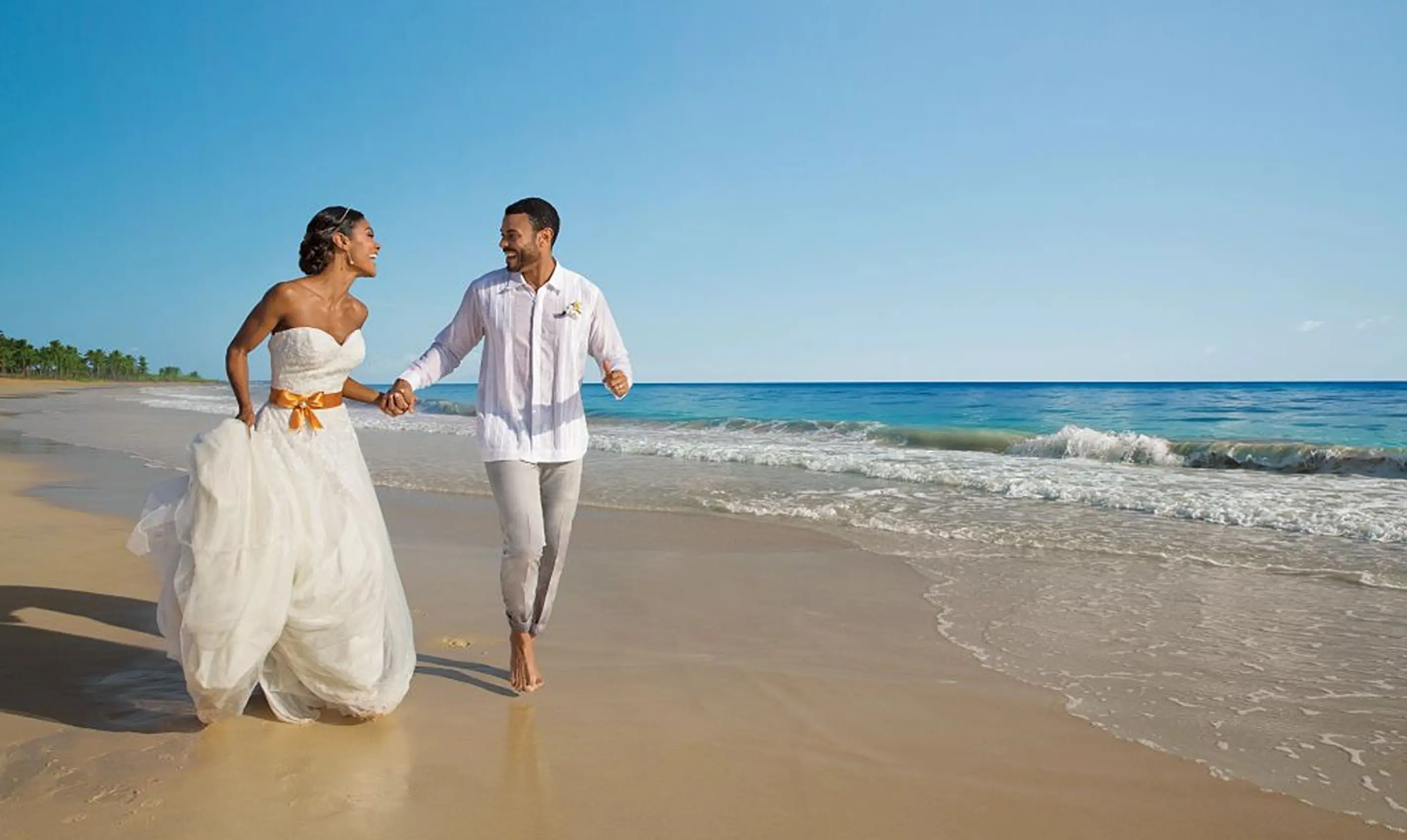 Bride and groom holding hands and running on the beach at Dreams Playa Esmeralda, Miches