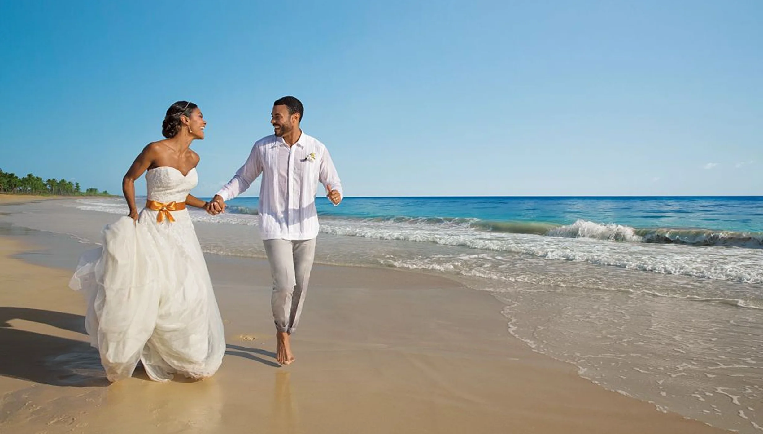 A joyful bride and groom, in wedding attire, holding hands and running along the beautiful sandy beach.