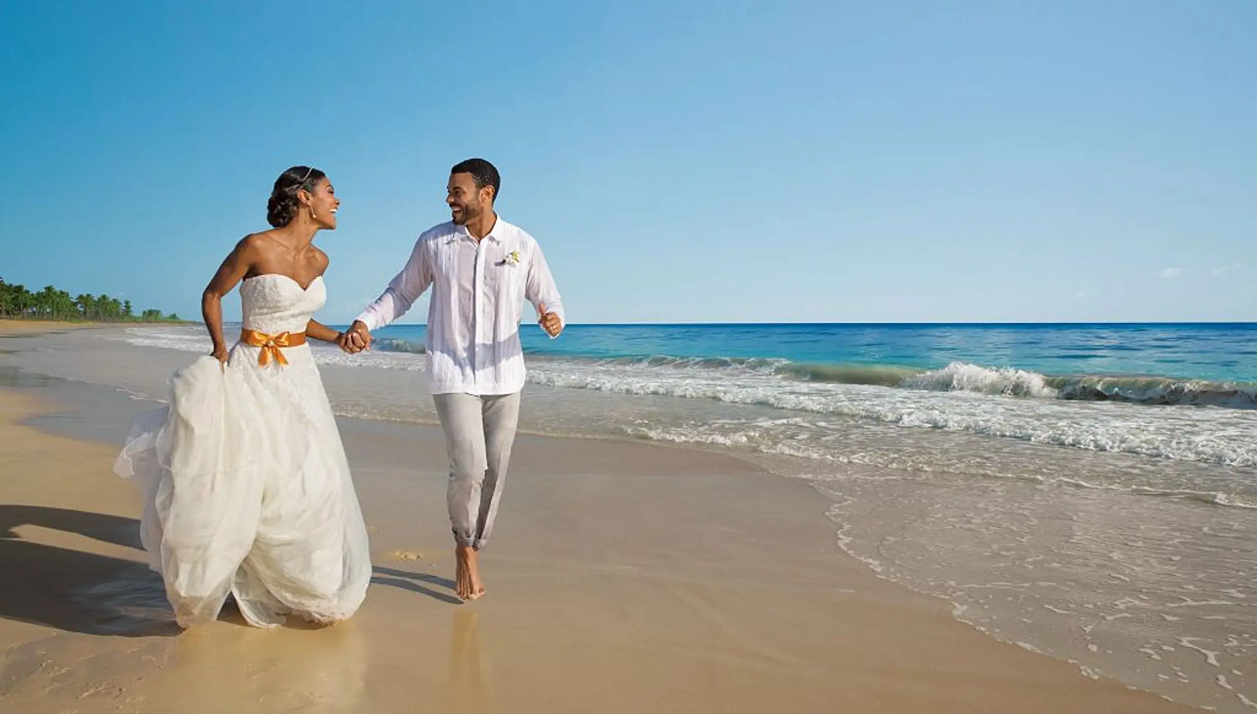 Bride and groom holding hands and running on the beach at Dreams Playa Esmeralda, Miches
