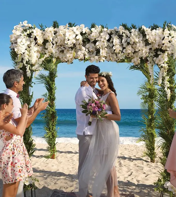 Bride and groom under a floral arch during a beach ceremony at Dreams Playa Esmeralda, Miches