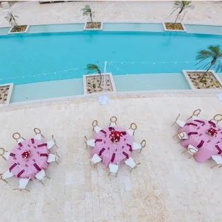An outdoor terrace with three tables set for a dinner, overlooking a beautiful turquoise blue swimming pool.