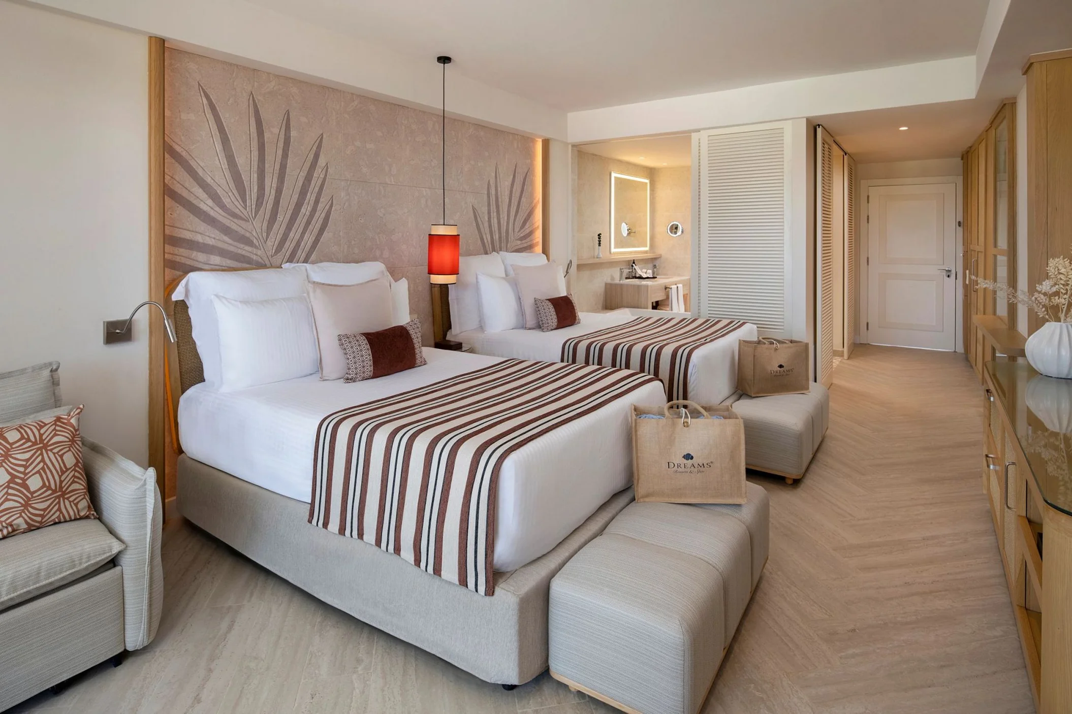 A luxurious hotel room with two beds, a tropical-inspired wall, and a view into the bathroom area.