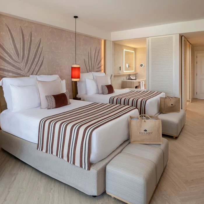 A luxurious hotel room with two beds, a tropical-inspired wall, and a view into the bathroom area.