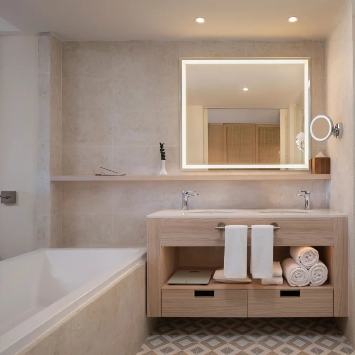 A bathroom with a double vanity, a large illuminated mirror, a bathtub, and a separate glass-enclosed shower.