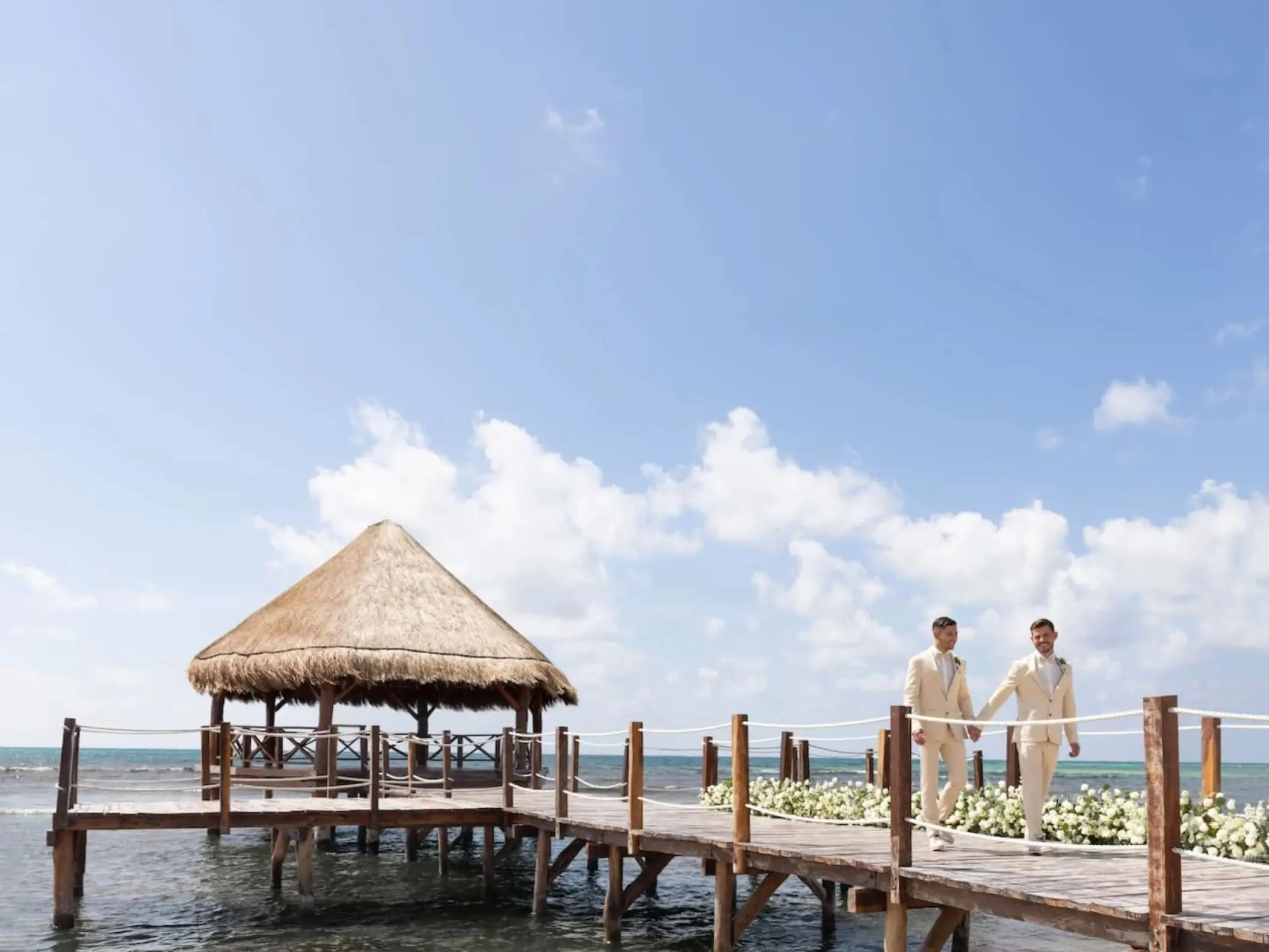 Two grooms walking along the overwater gazebo pier at Dreams Puerto Morelos, Riviera Maya