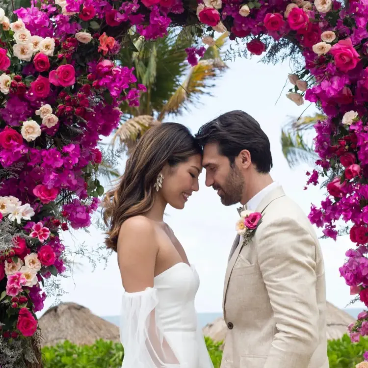 Bride and groom touching foreheads under a pink floral arch at Dreams Puerto Morelos, Riviera Maya
