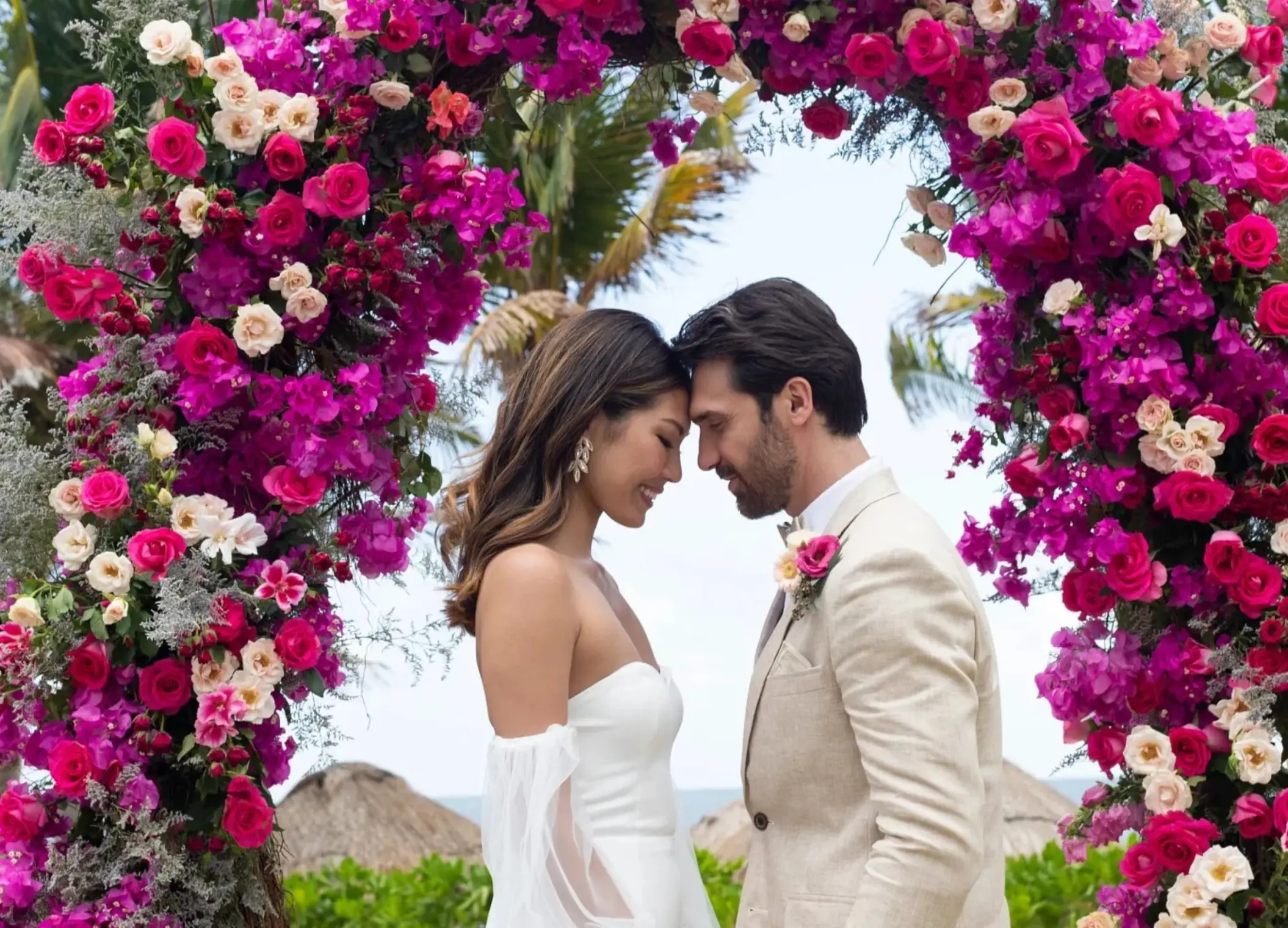 Bride and groom touching foreheads under a pink floral arch at Dreams Puerto Morelos, Riviera Maya