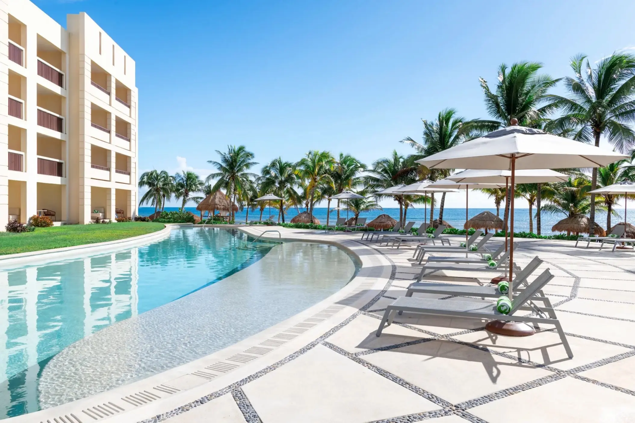 Poolside loungers and umbrellas beside a winding swimming pool at Dreams Puerto Morelos, Riviera Maya