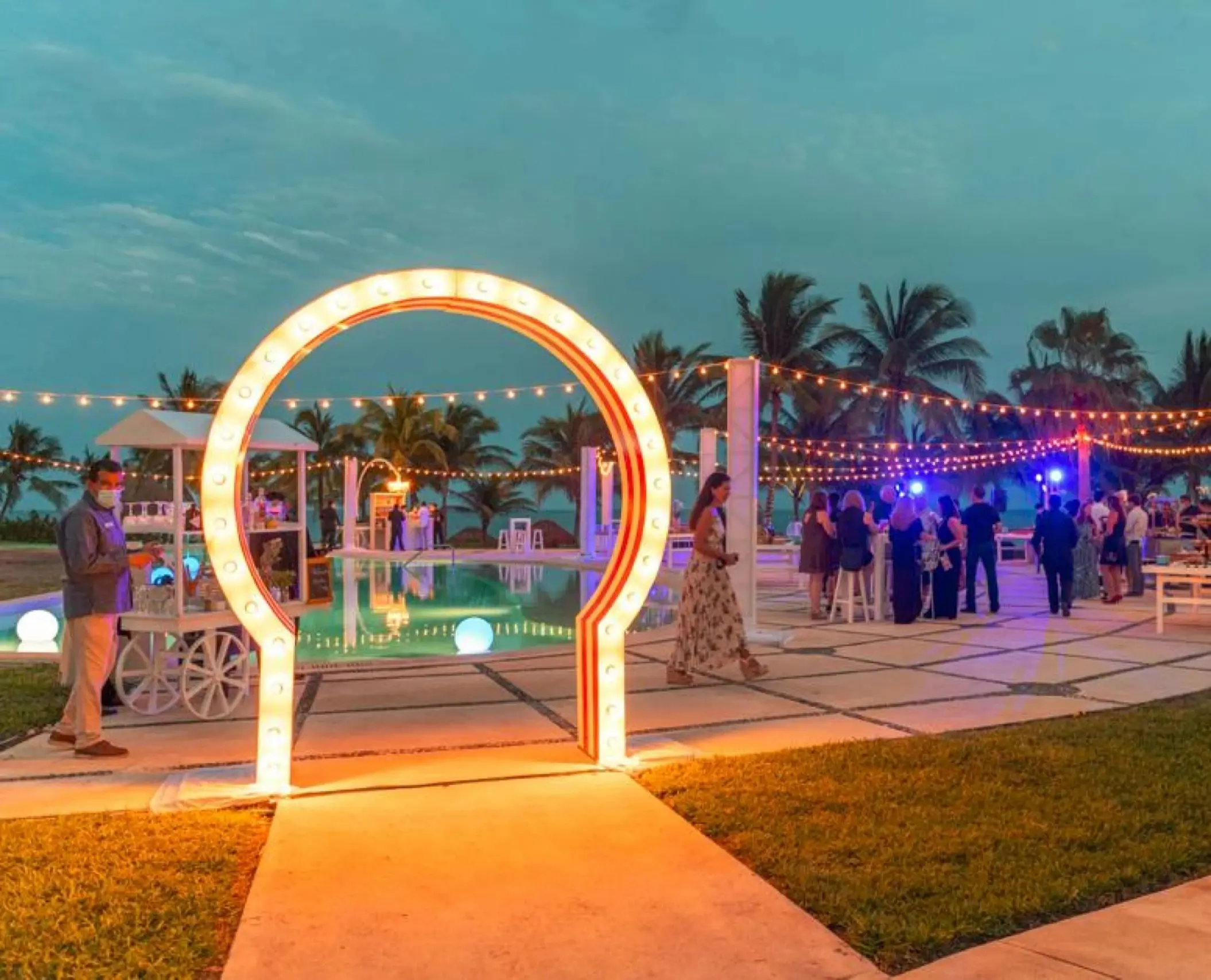 Pool deck wedding reception at Dreams Puerto Morelos, Riviera Maya featuring a light-up arch and string lights