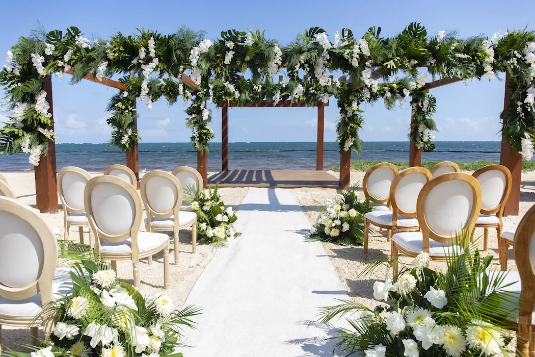 Beachfront wedding ceremony with floral pergola and white aisle at Secrets Riviera Cancun, Riviera Maya