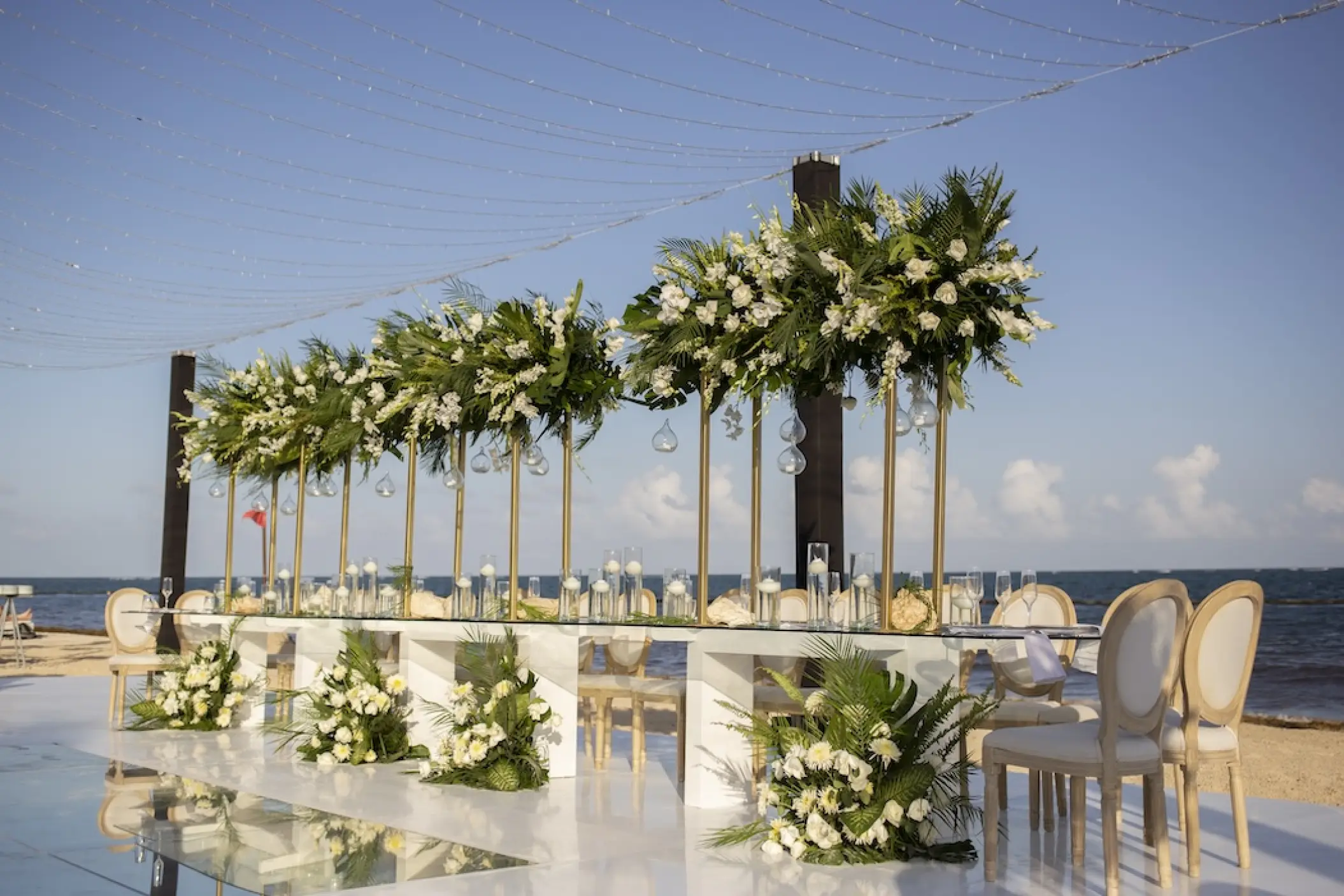 Long wedding reception table with white floral centerpieces on the beach at Secrets Riviera Cancun, Riviera Maya