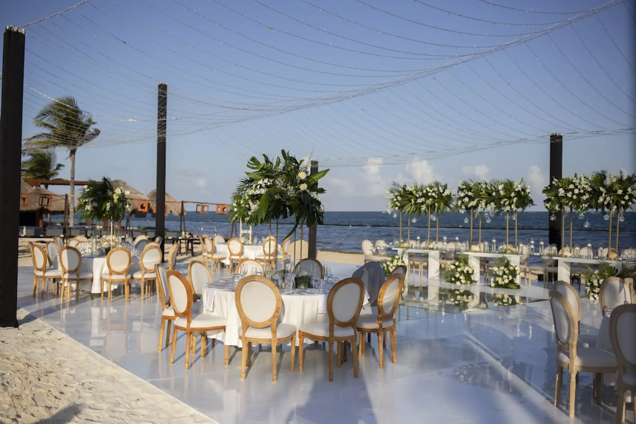 Beachfront wedding reception with white dance floor and floral centerpieces at Dreams Riviera Cancun, Riviera Maya