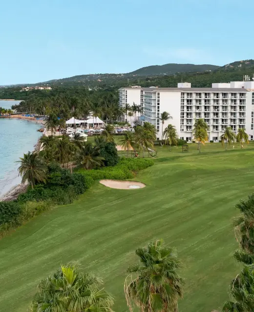 Aerial view of the Dreams Rose Hall Resort & Spa, showcasing the hotel buildings, ocean, and lush green golf course.