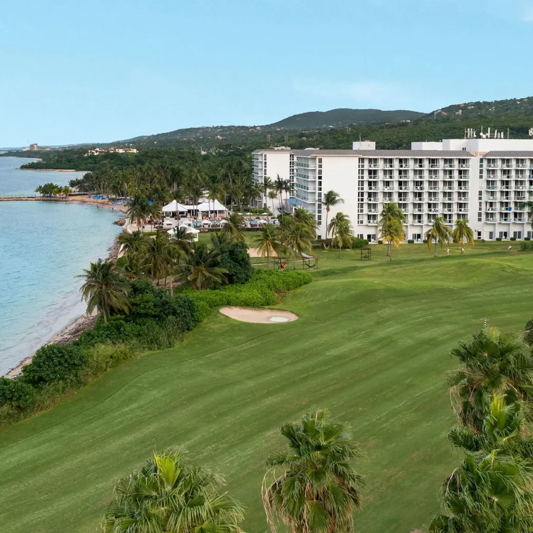 Aerial view of the Dreams Rose Hall Resort & Spa, showcasing the hotel buildings, ocean, and lush green golf course.
