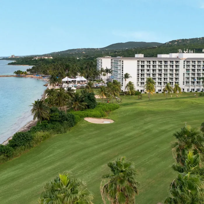 Aerial view of the Dreams Rose Hall Resort & Spa, showcasing the hotel buildings, ocean, and lush green golf course.