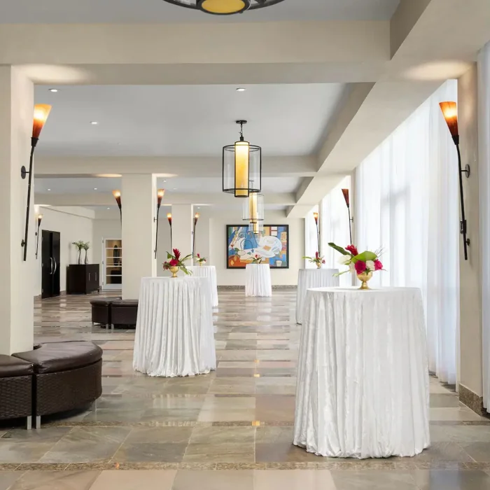 A cocktail set-up in the spacious ballroom foyer of Dreams Rose Hall, with white-draped tables and lighting.