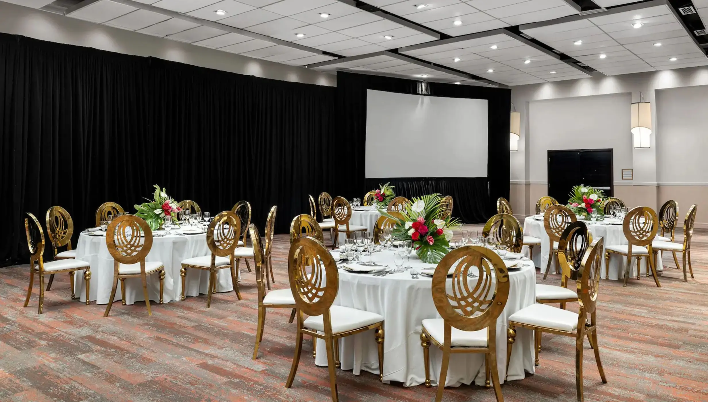 The beautifully set-up ballroom venue at the resort, featuring round tables, elegant gold chairs, and a screen.