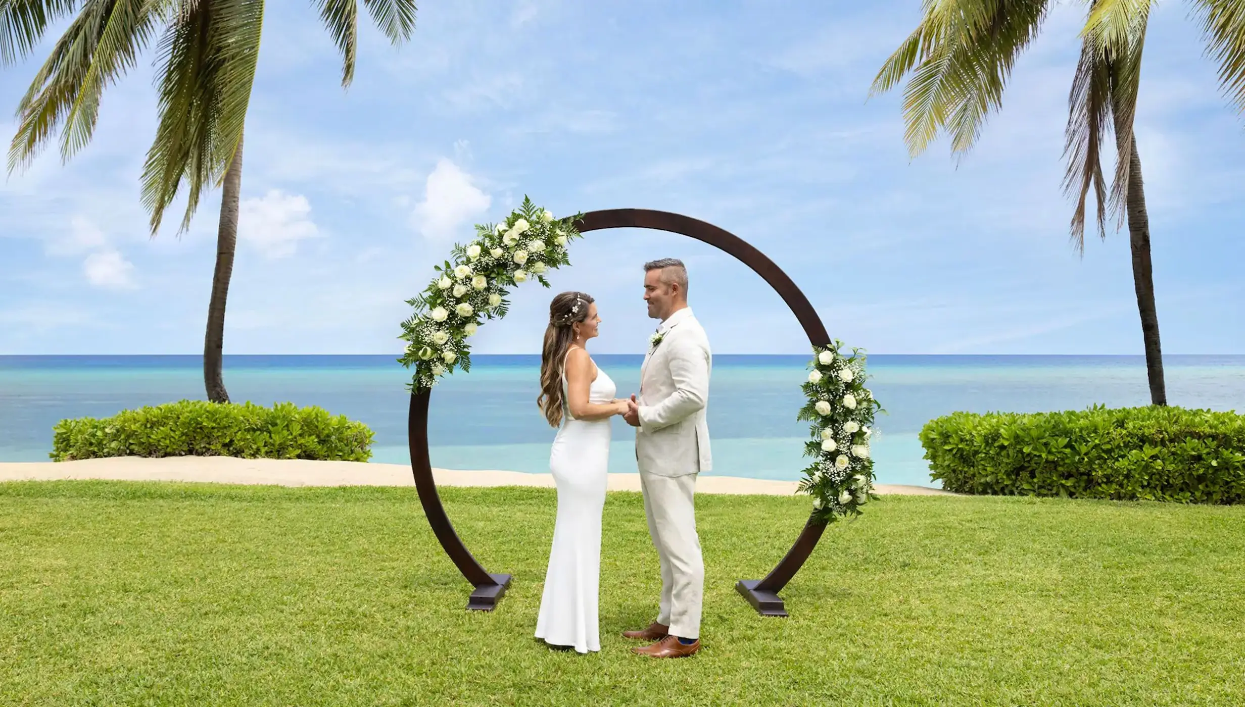 A bride and groom standing at the resort's West Lawn wedding venue with the ocean in the background.