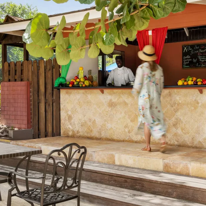 The resort's outdoor Jerk Hut with a bartender, a guest, and a selection of fresh fruits on the counter.