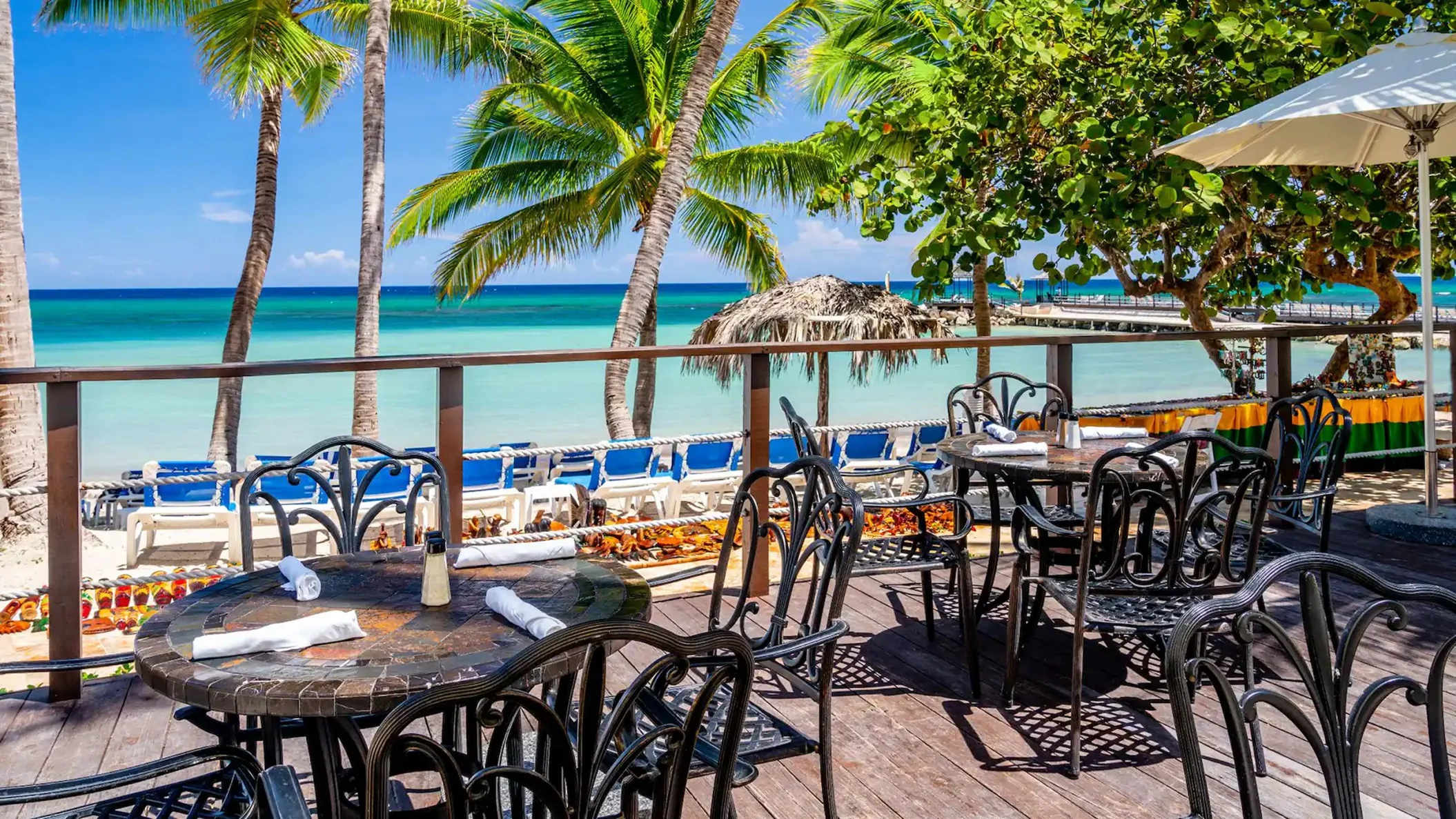 Outdoor seating at Mangoes Restaurant, with tables on a deck and a beautiful view of the beach and ocean.