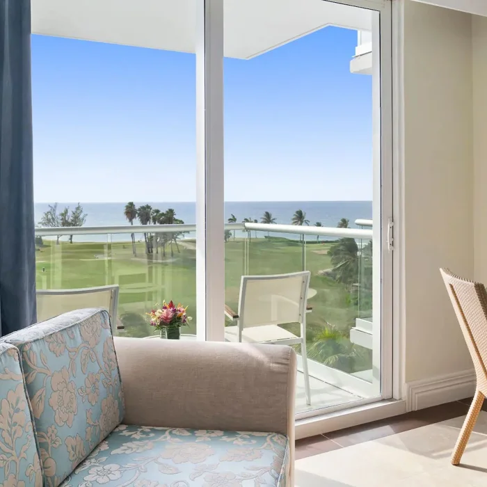 Living area of a Partial Ocean View King room with a sofa and desk, looking out onto a balcony and the ocean.