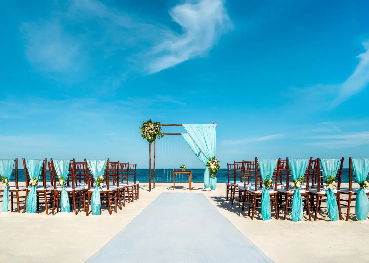 Beachfront wedding ceremony with turquoise chair sashes and floral arch at Dreams Royal Beach, Punta Cana
