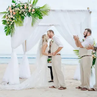 The couple kissing at a beach ceremony under a white draped gazebo at Dreams Royal Beach, Punta Cana