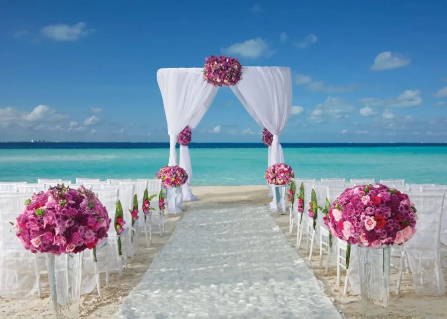 Beachfront wedding ceremony with white arch and pink floral arrangements at Dreams Sands Cancun, Cancun