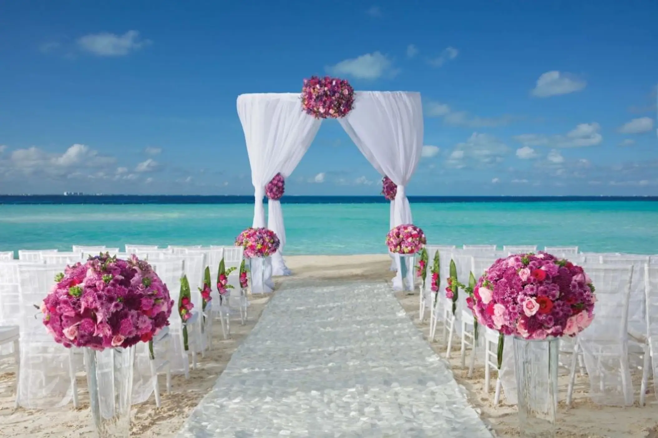 Beachfront wedding ceremony with white arch and pink floral arrangements at Dreams Sands Cancun, Cancun