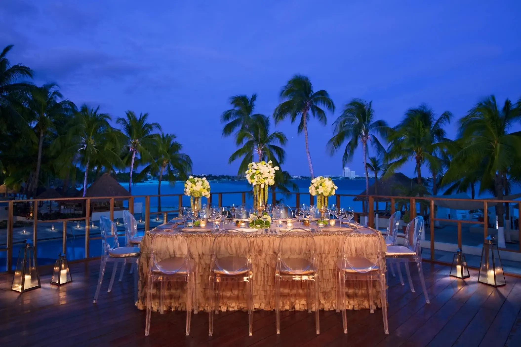 Evening wedding reception setup with clear chairs and floral centerpieces at Dreams Sands Cancun, Cancun
