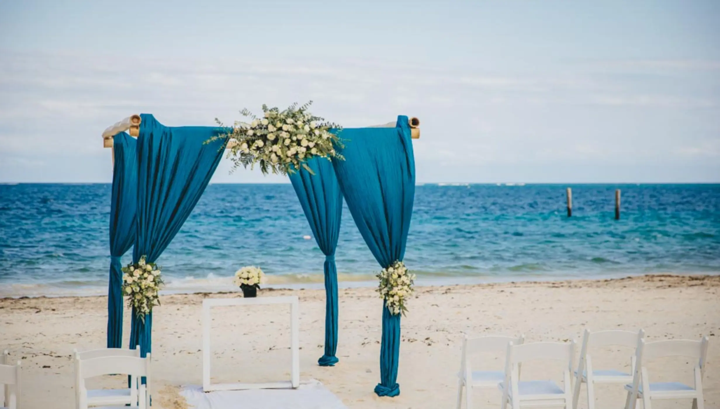 Beach wedding ceremony arch with teal fabric and white flowers at Dreams Sapphire, Riviera Maya