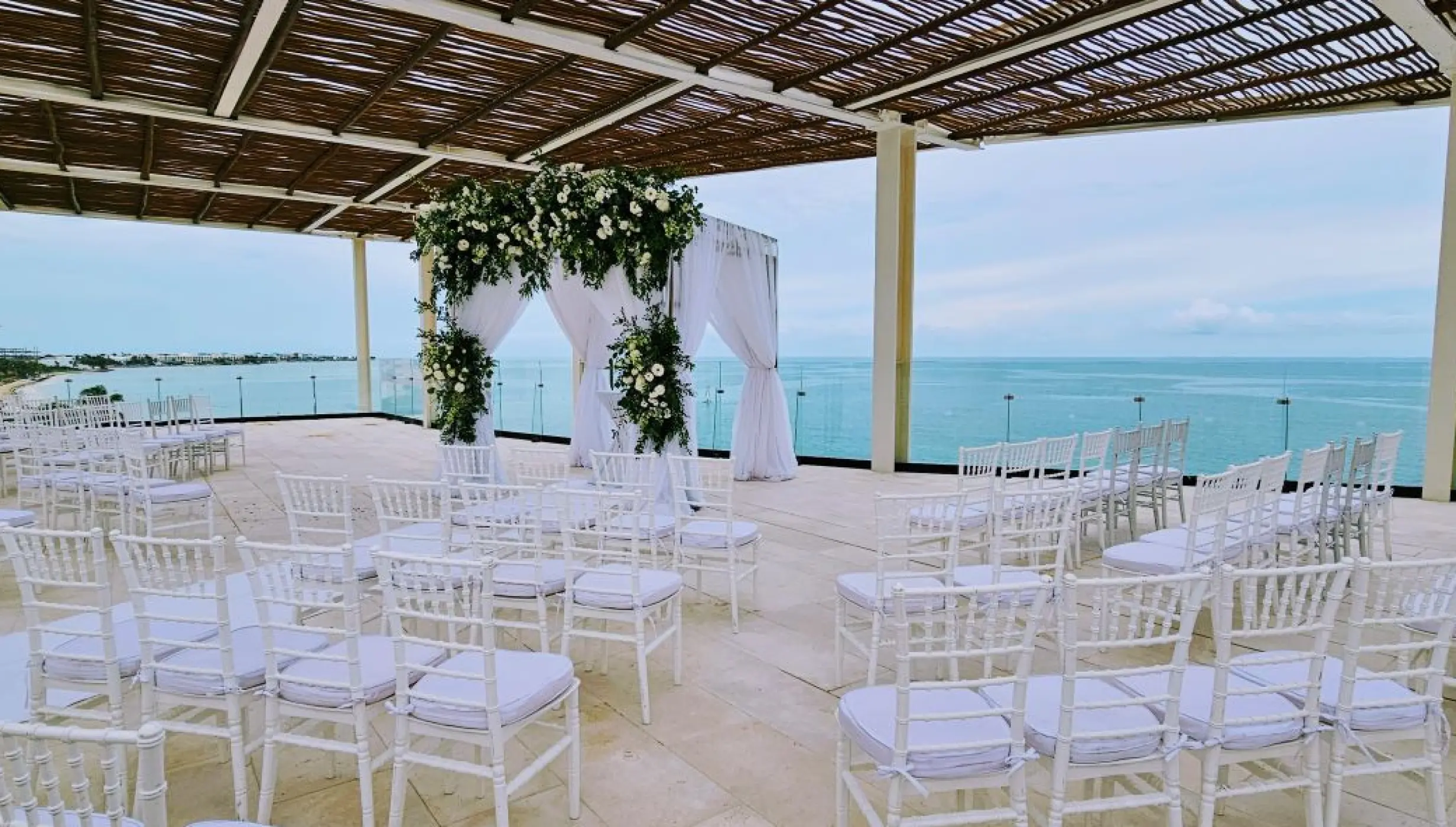 Rooftop wedding ceremony at Dreams Sapphire, Riviera Maya featuring white chairs and a floral arch overlooking the ocean