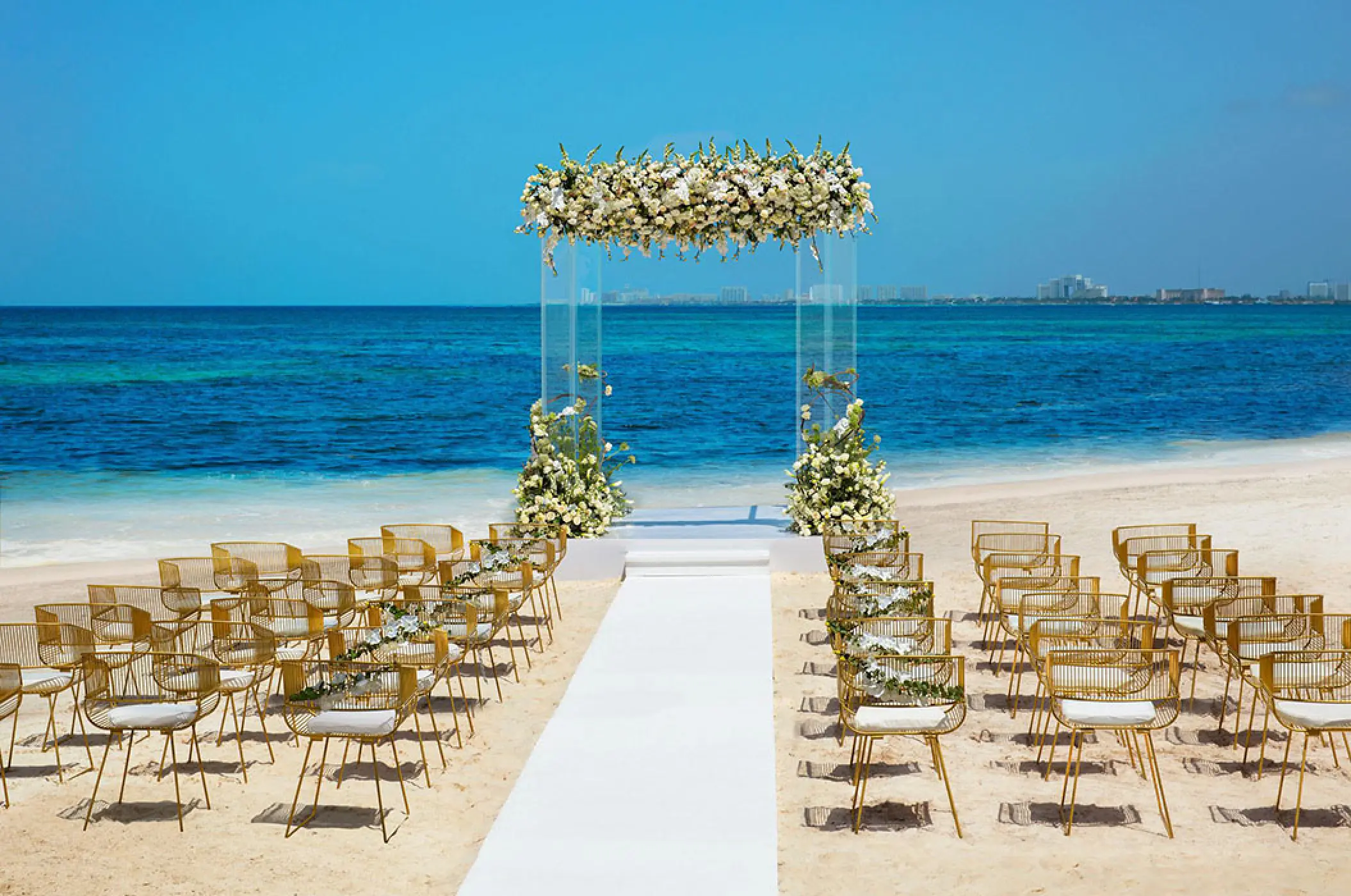 Beachfront wedding ceremony with acrylic arch and gold chairs at Dreams Vista Cancun