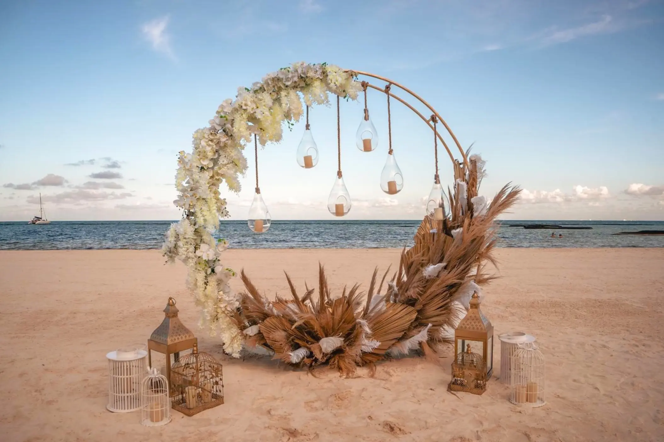 Beachfront wedding ceremony circular arch with pampas grass and hanging lanterns at El Dorado Maroma, Riviera Maya
