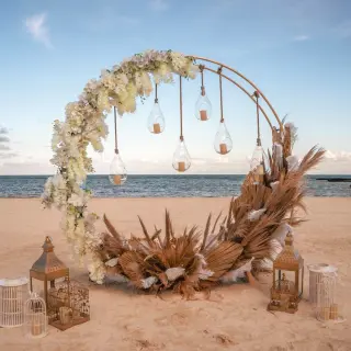 Beachfront wedding ceremony circular arch with pampas grass and hanging lanterns at El Dorado Maroma, Riviera Maya