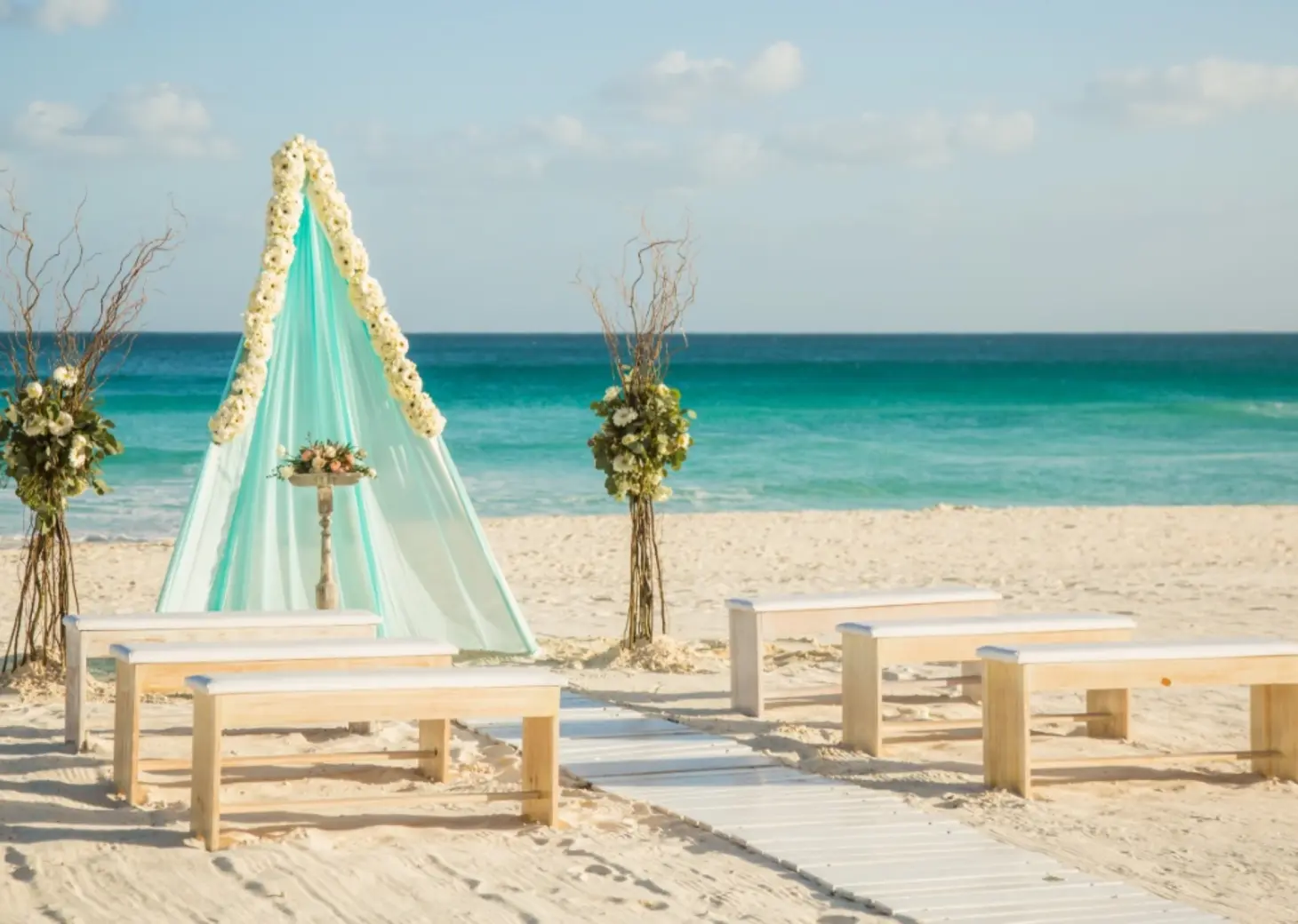 Beachfront wedding ceremony setup with teepee arch and wooden benches at El Dorado Palafitos, Riviera Maya