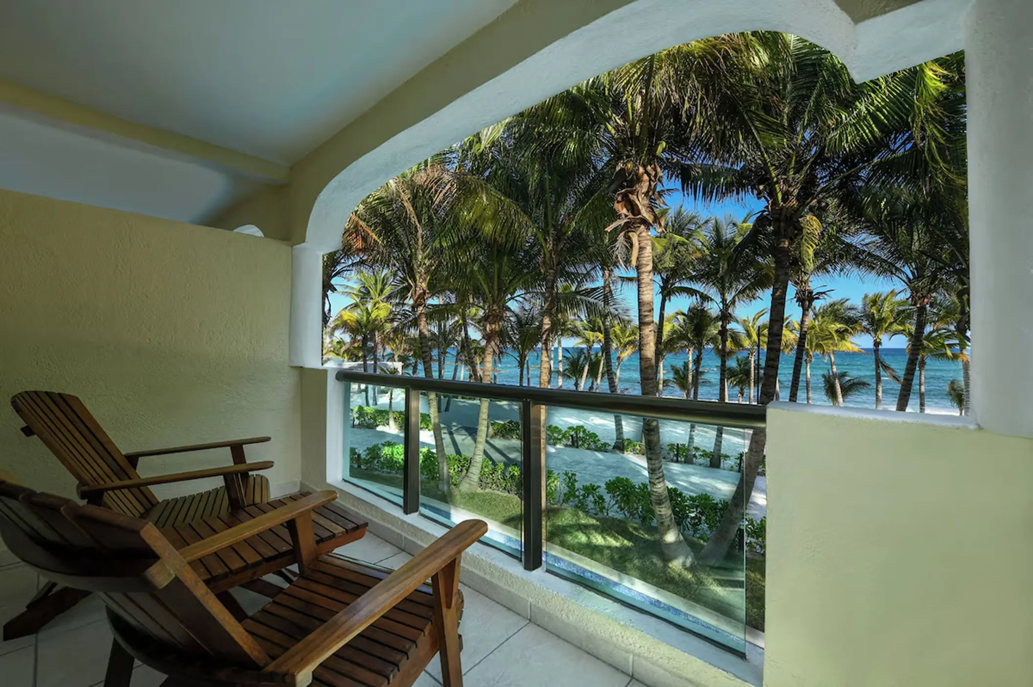 Suite balcony with wooden lounge chairs overlooking palm trees and the ocean at El Dorado Royale, Riviera Maya