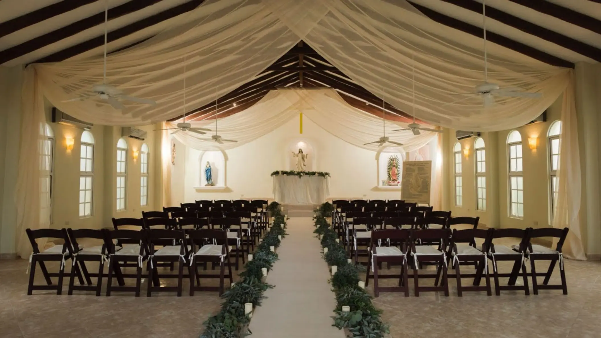Indoor wedding ceremony at El Dorado Royale, Riviera Maya, featuring a draped ceiling and wooden aisle chairs