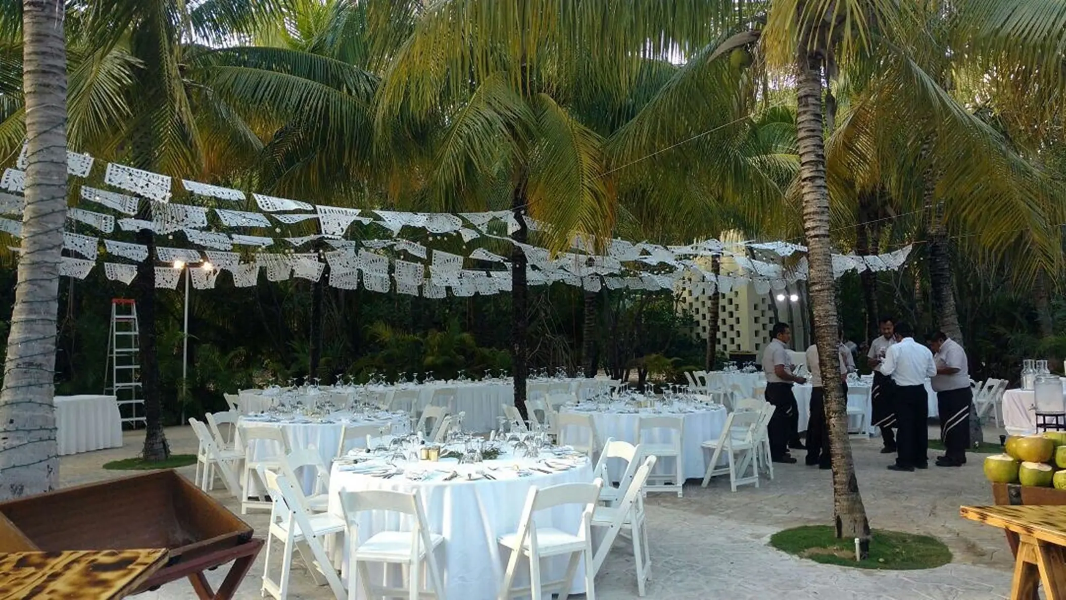 Outdoor wedding reception under palm trees and white papel picado banners at El Dorado Royale, Riviera Maya