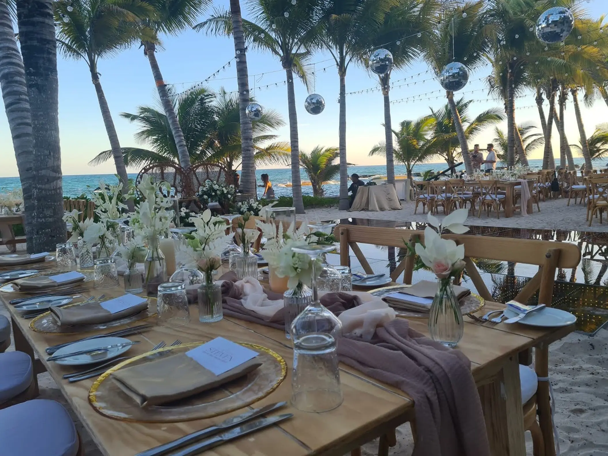 Outdoor beach reception with wooden tables, disco balls and palm trees at El Dorado Royale, Riviera Maya
