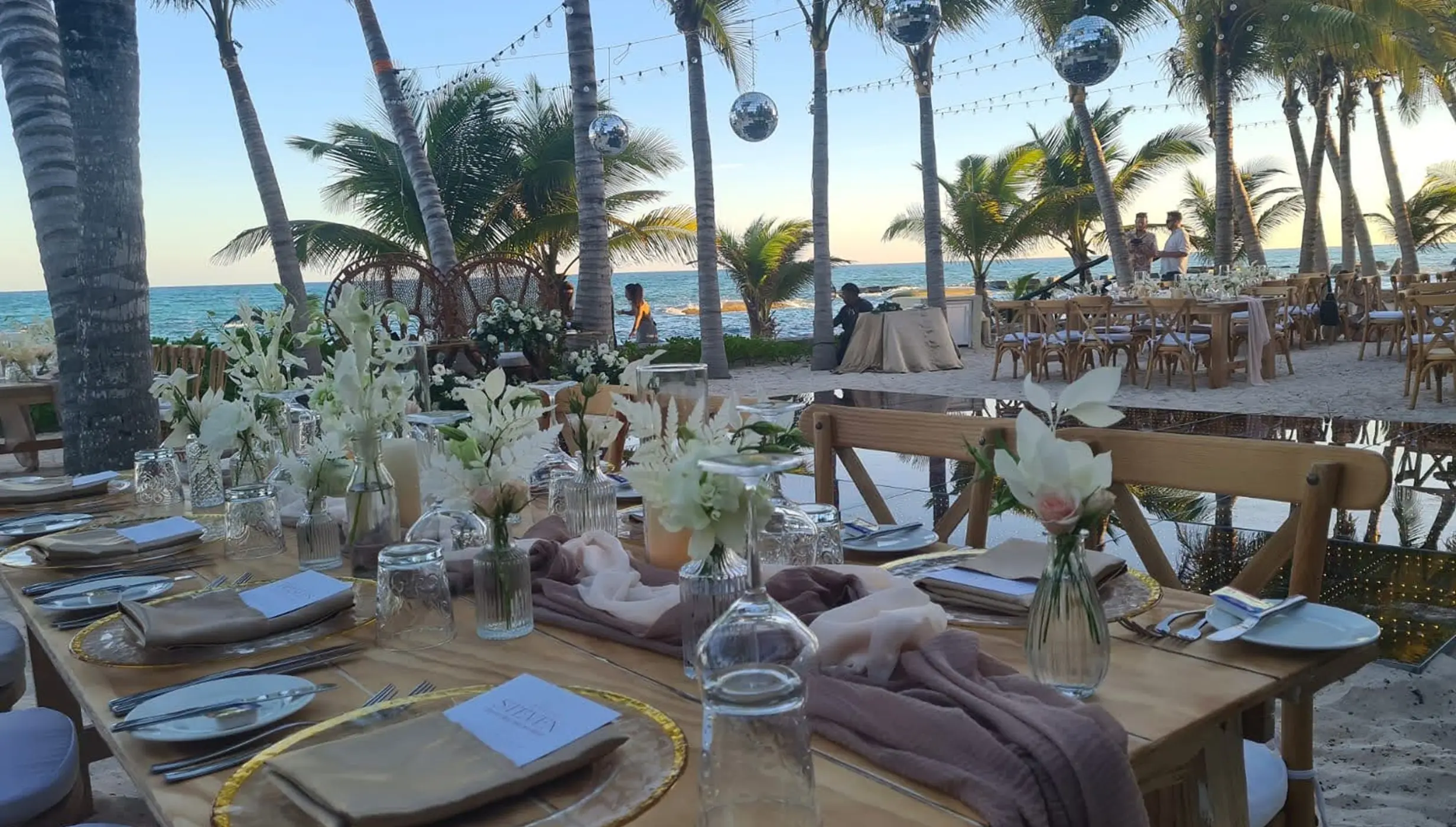 Outdoor beach reception with wooden tables, disco balls and palm trees at El Dorado Royale, Riviera Maya
