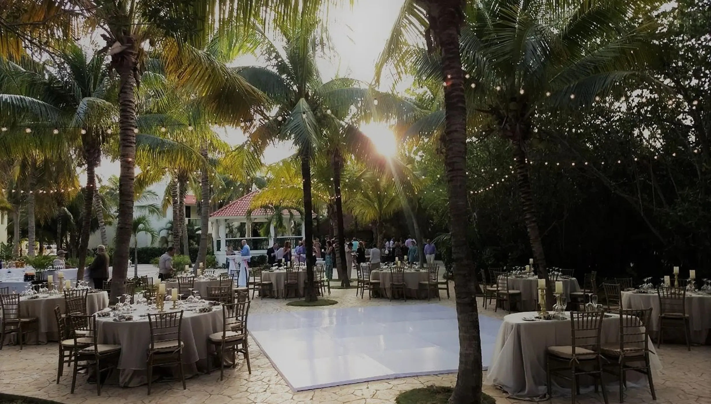 Outdoor wedding reception with white dance floor and string lights under palm trees at El Dorado Royale, Riviera Maya