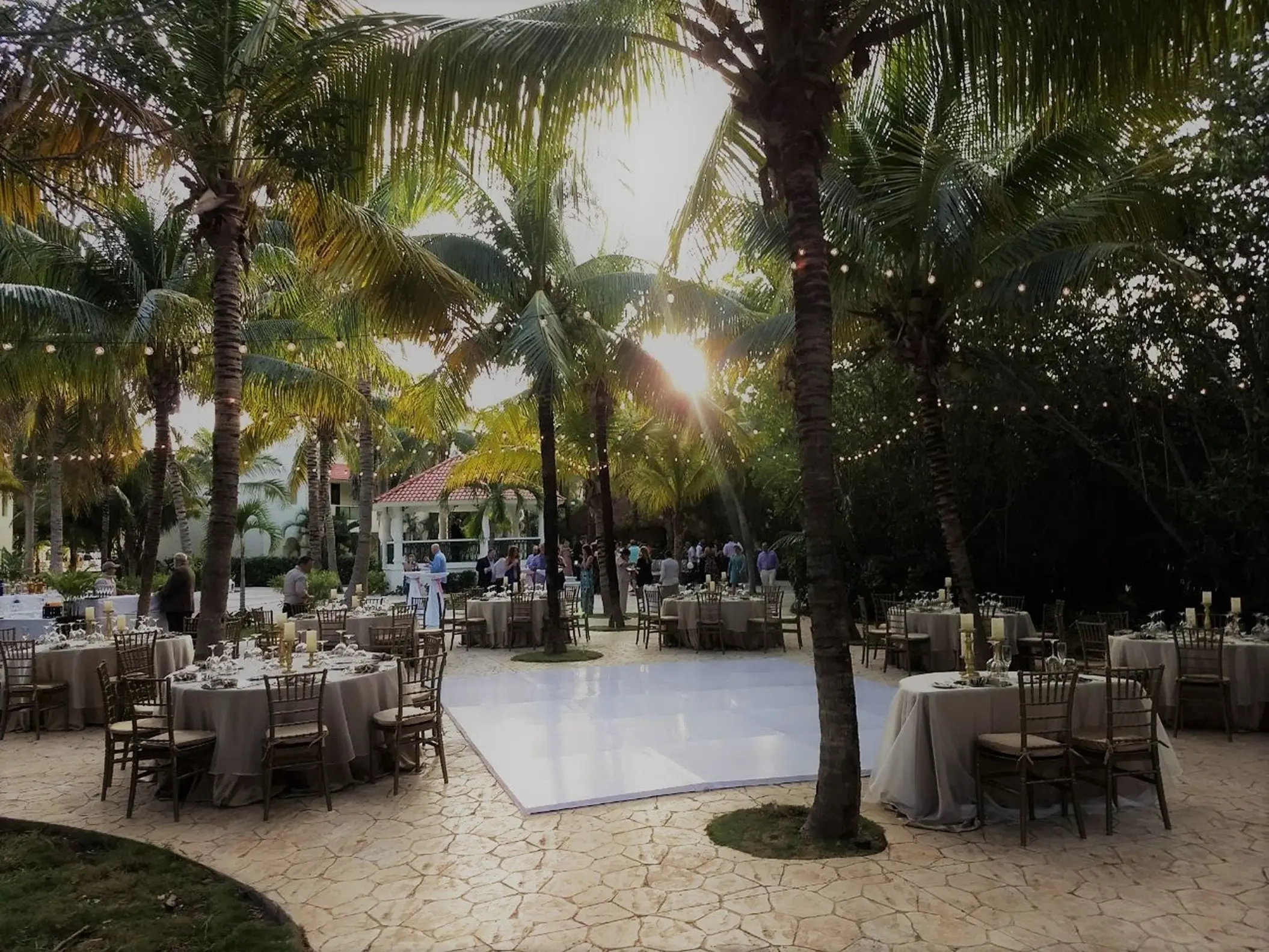 Outdoor wedding reception with white dance floor and string lights under palm trees at El Dorado Royale, Riviera Maya