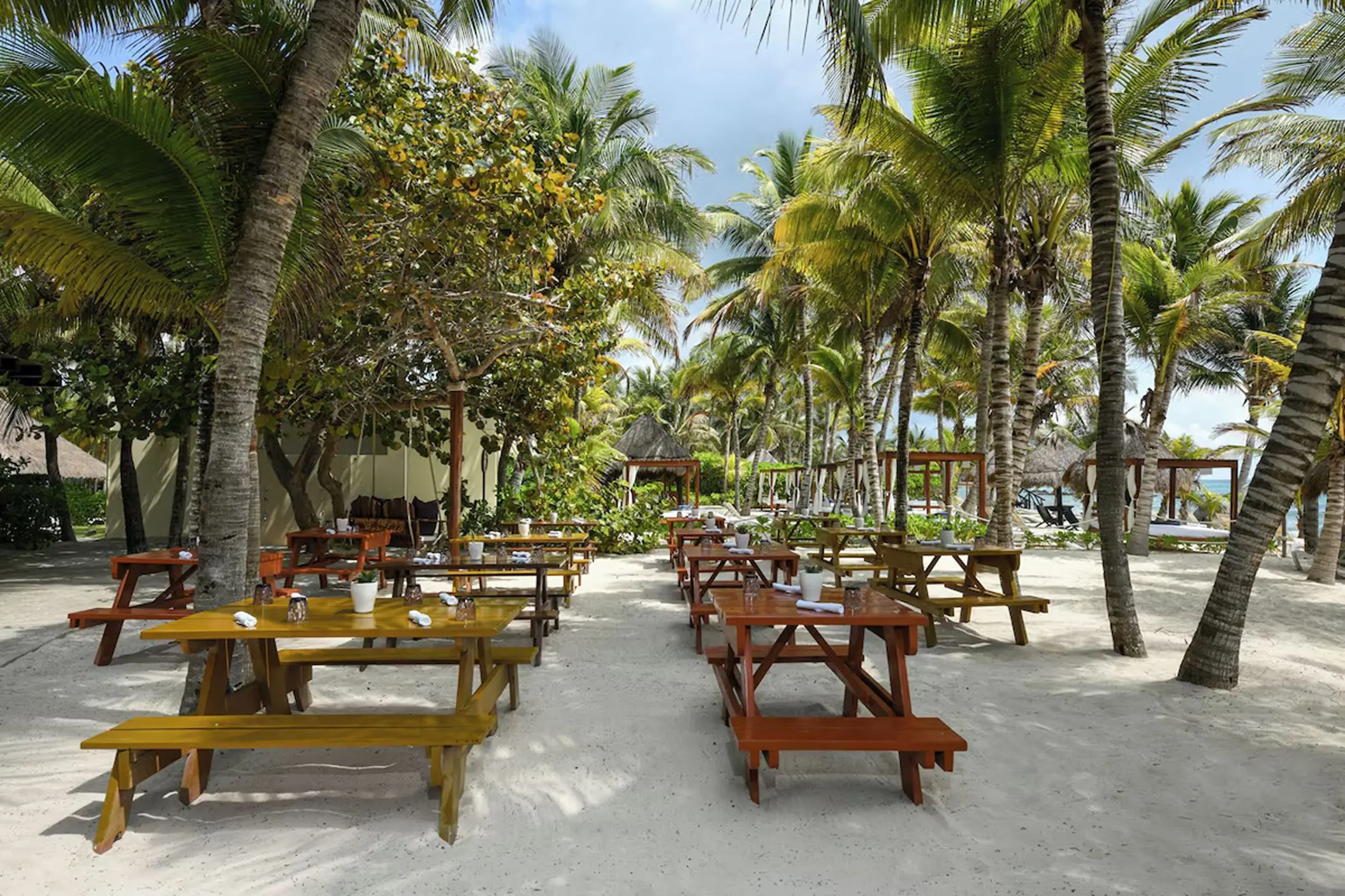 Outdoor dining area with wooden picnic tables under palm trees at El Dorado Royale, Riviera Maya