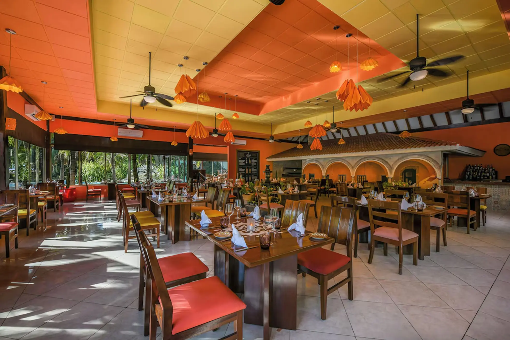 Colorful gourmet restaurant with orange accents and ceiling fans at El Dorado Royale, Riviera Maya