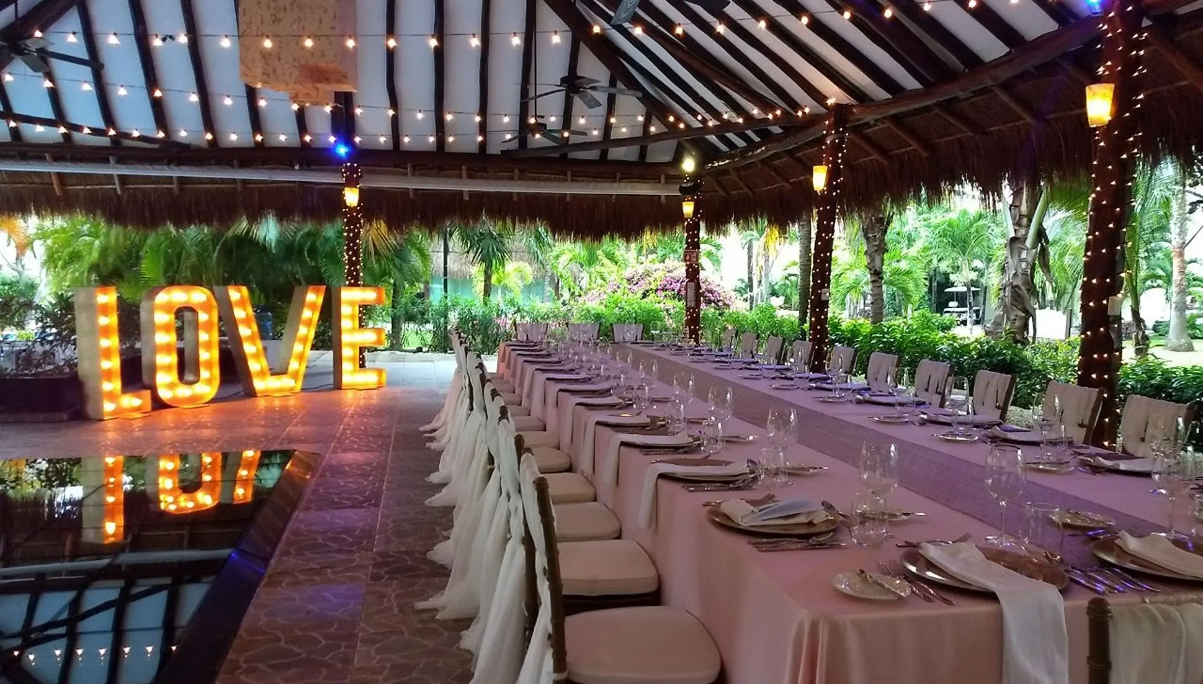 Long banquet table wedding reception under a palapa with illuminated LOVE sign at El Dorado Royale, Riviera Maya