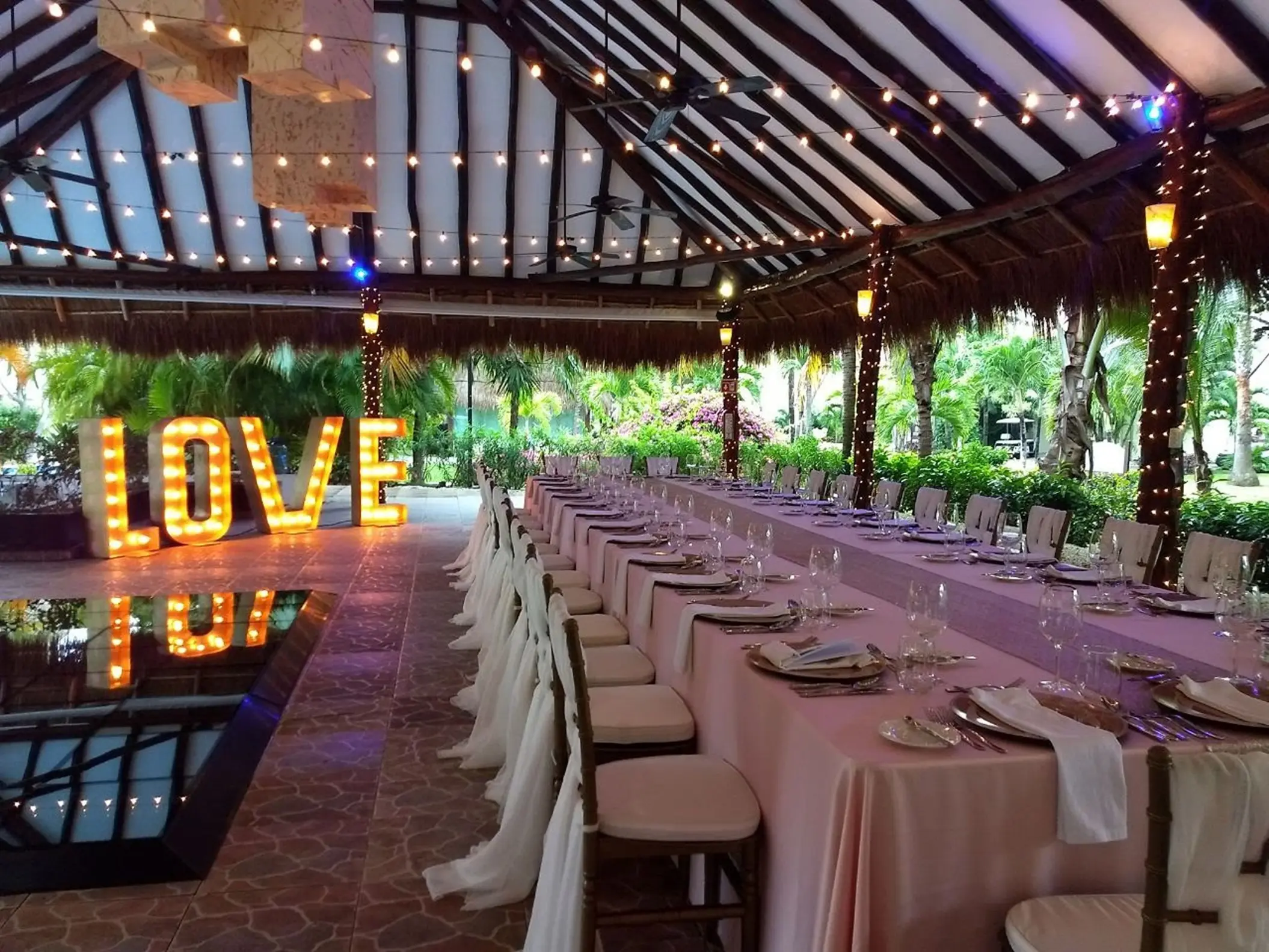 Long banquet table wedding reception under a palapa with illuminated LOVE sign at El Dorado Royale, Riviera Maya