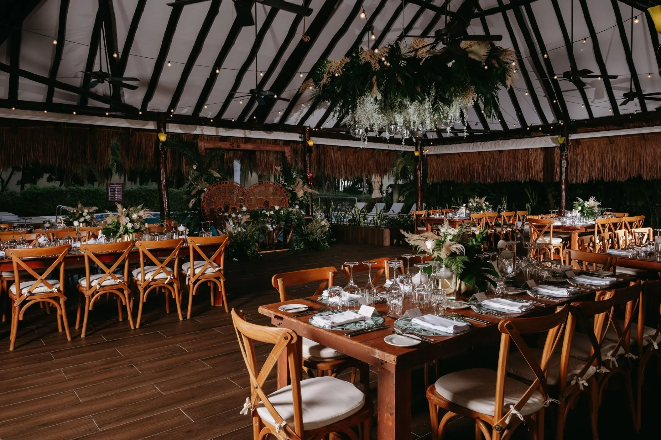 Indoor wedding reception under a palapa with wooden cross-back chairs at El Dorado Royale, Riviera Maya